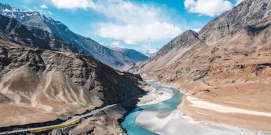 A river winding through a rugged mountain valley under a partly cloudy sky.