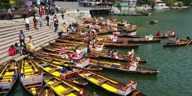 Colorful wooden boats docked by the river with people boarding and walking nearby.
