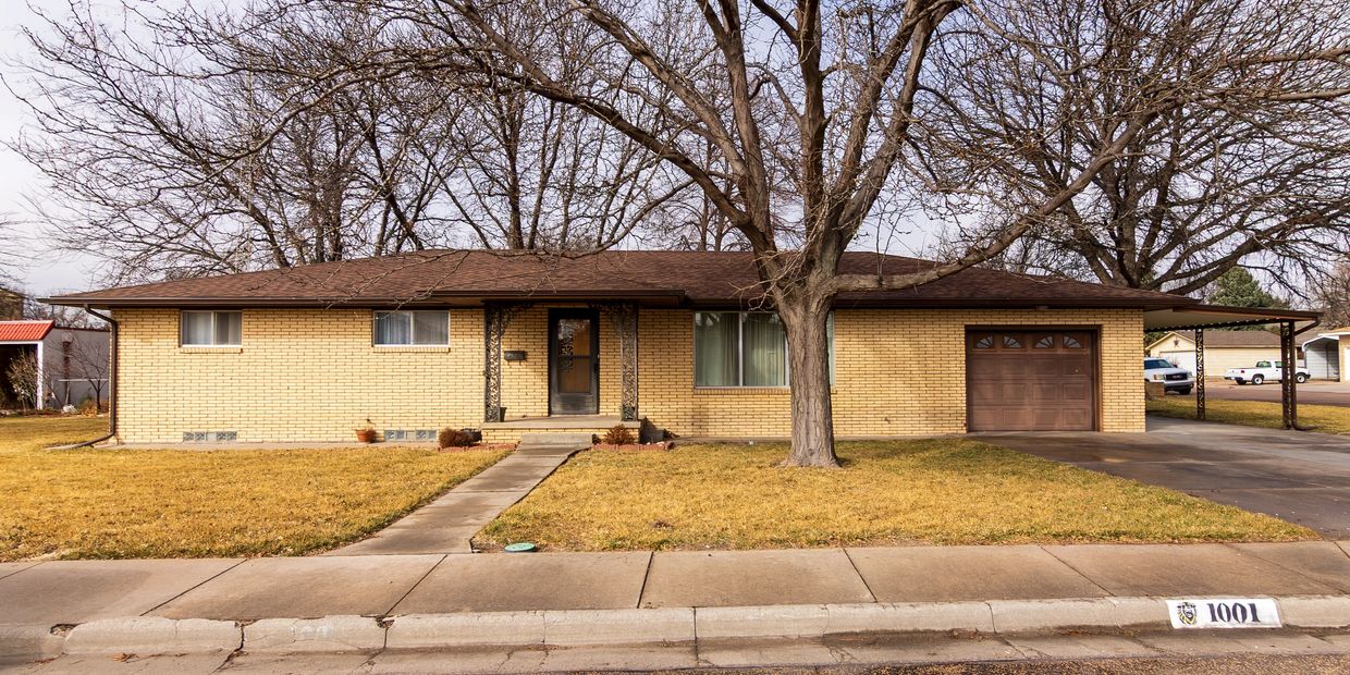 Single-story brick house with a brown roof and large tree in front yard.