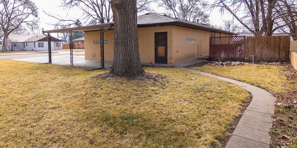 Small brick house with a large tree and a curved sidewalk.