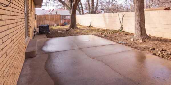 Empty backyard with cracked concrete and bare trees.