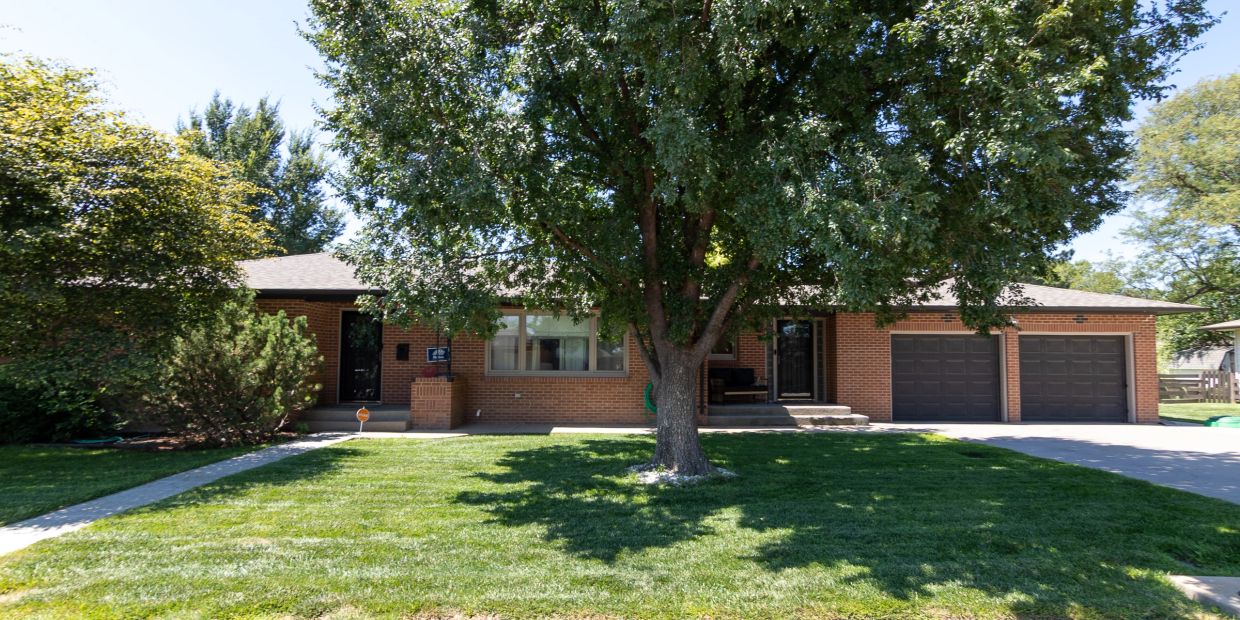 Brick house with large tree and green lawn.