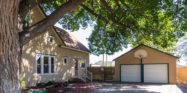 House with large tree and double garage under bright sunlight.