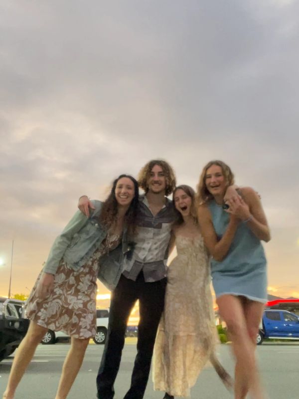 Four friends smiling and posing together outdoors at sunset.