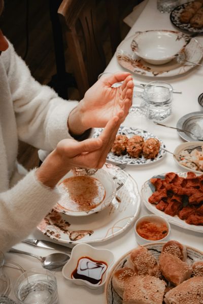 Person gesturing during a shared meal at a table filled with a variety of dishes, reflecting connect