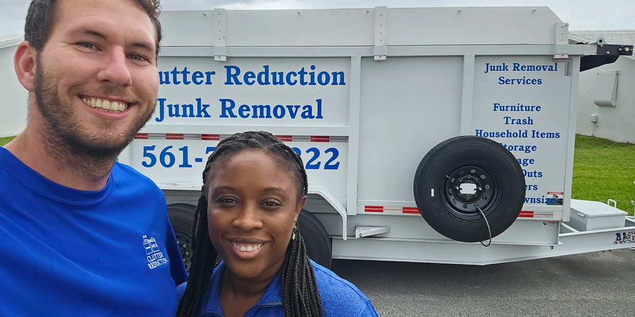 Two smiling people in front of a clutter reduction junk removal trailer.