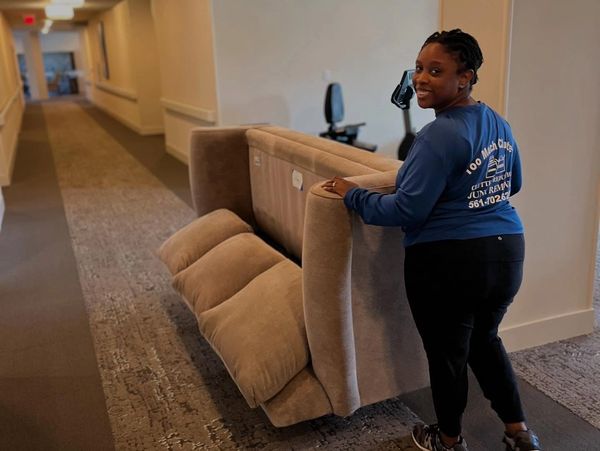 Woman smiling while pushing a couch on a dolly through a hallway