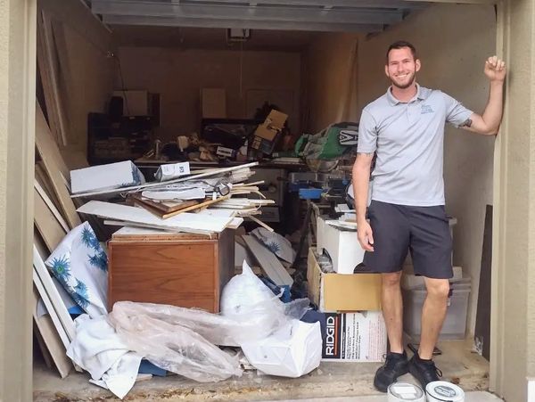 Man smiling in front of a garage full of trash and debris