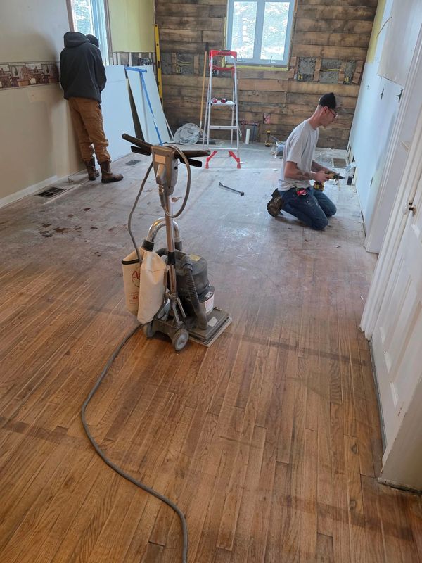 Two men doing home renovation with a floor sander in the foreground.