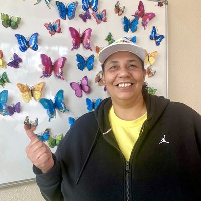 Smiling person posing with colorful butterfly decorations on a whiteboard.