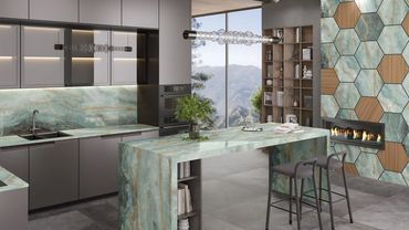 Modern kitchen with marble countertops and hexagonal wall tiles beside a fireplace.