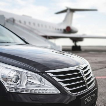 Luxury black car parked near a private jet on an airstrip.