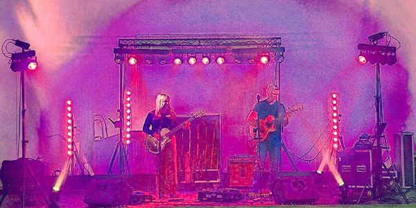 Two musicians perform on stage with vibrant purple and pink lighting.