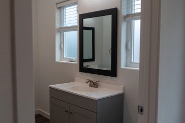 Modern bathroom sink with a black-framed mirror and frosted windows.
