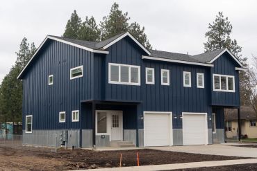 Modern blue duplex house with white garages and metal siding.