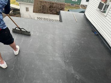 Person sweeping a flat roof with tools scattered around.