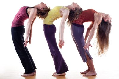 Three women doing standing backbends, each leaning on the next one