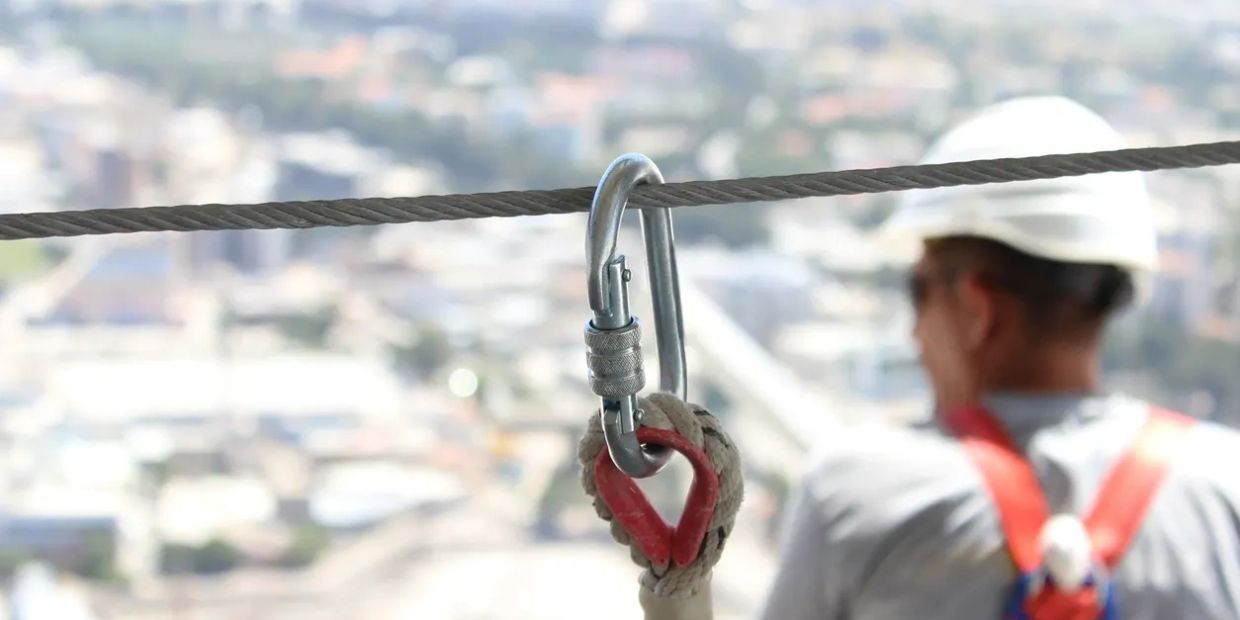 Safety clip attached to a cable with a blurred worker in the background.