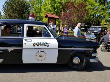 Vintage black and white police car with people around during a sunny day event.