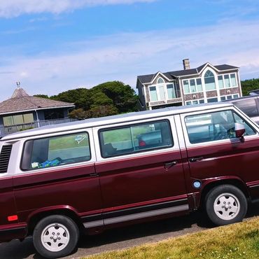 Maroon and white vintage van parked on a street near houses under a blue sky.