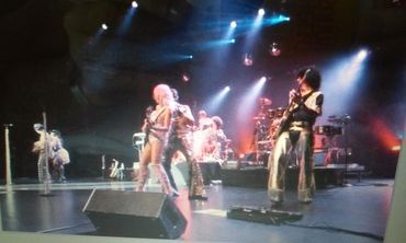 A lively band performs on stage with bright lights and flashy outfits.