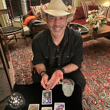 Man in a cowboy hat smiling while reading tarot cards.
