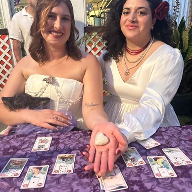 Two women engaging in a tarot card reading with a heart-shaped stone.