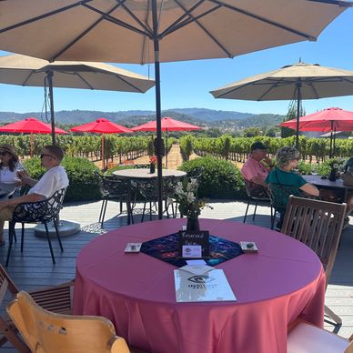 Outdoor winery seating with umbrellas and vineyard view.