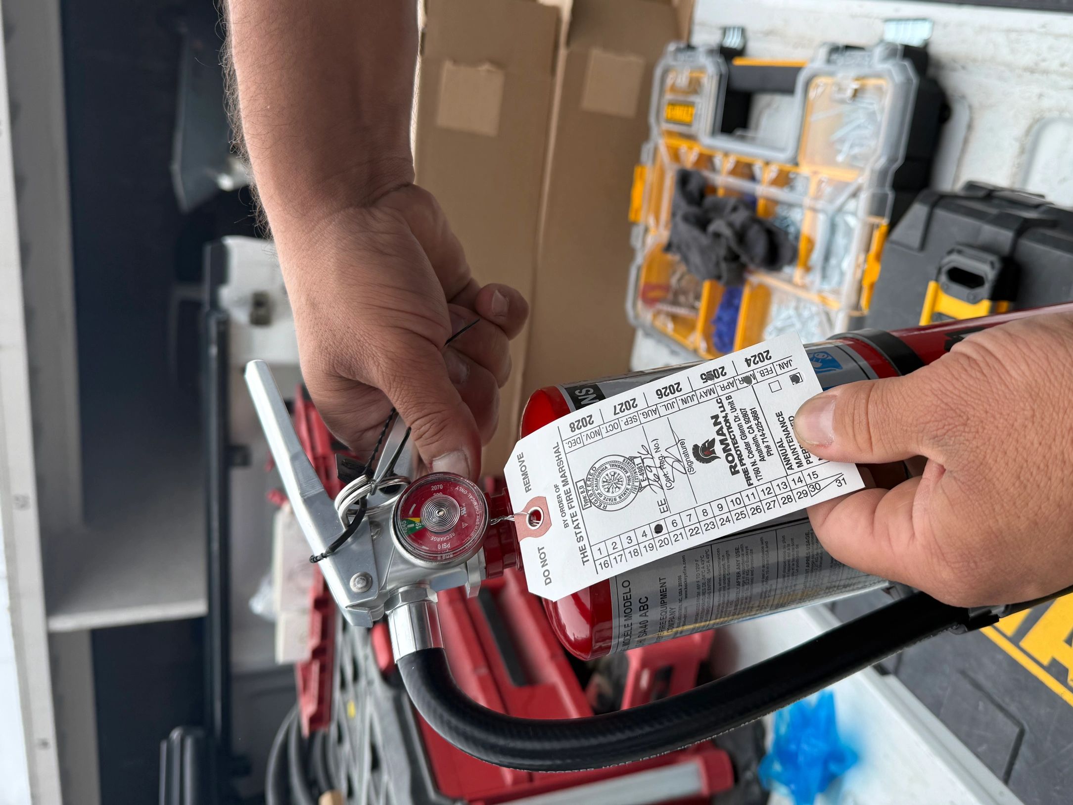 Hands holding a fire extinguisher with an inspection tag.
