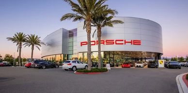 Modern Porsche dealership with palm trees at sunset.