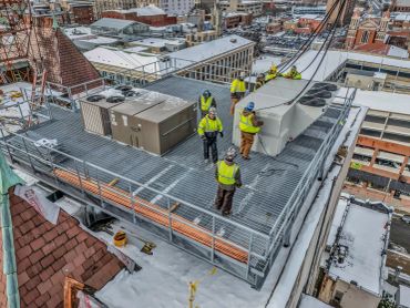 Construction workers installing HVAC units on a rooftop in a snowy urban area.