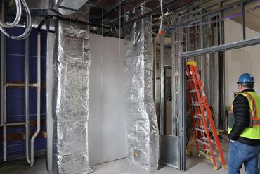 Construction worker inspecting ductwork in a building under renovation.