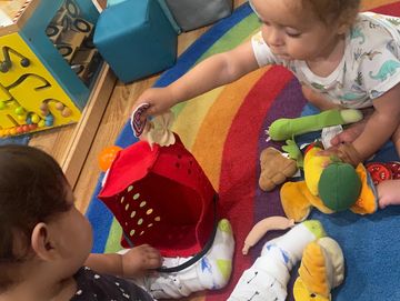 Infants playing on the rainbow rug, placing materials in basket.