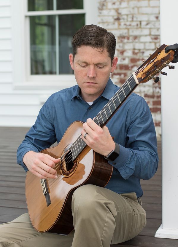 Aaron Prillaman playing classical guitar on a porch.