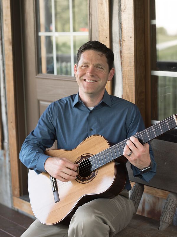 Aaron Prillaman playing classical guitar on a porch at the Triple J Manor House.