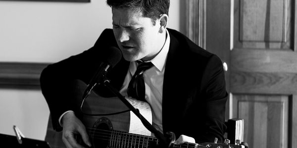 Aaron Prillaman playing the acoustic guitar and singing at a wedding reception.