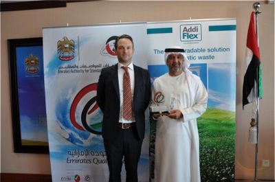 Two men at a formal event with Emirates Quality banners and UAE flag.