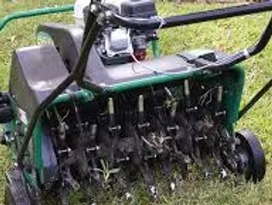 A motorized lawn aerator with multiple spikes on grass.