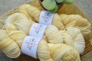 Three skeins of light yellow yarn on a yellow glass plate with a small plant.