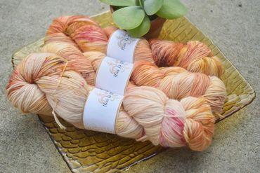 Three skeins of peach-toned yarn on a glass tray with a small succulent plant.