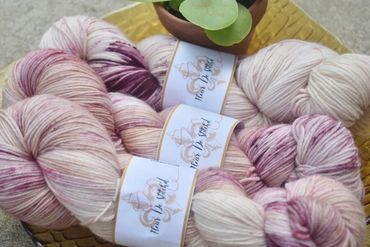 Skeins of pink and purple speckled yarn with labels, arranged near a small potted plant.