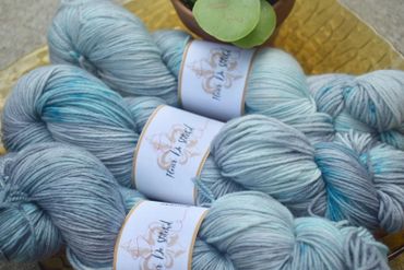 Soft blue and gray skeins of yarn with labels, arranged with a small plant.