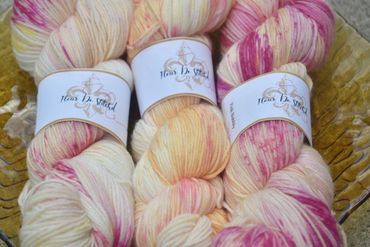 Three skeins of pastel-colored yarn with pink and yellow hues labeled 'Fleur De Stitched'.