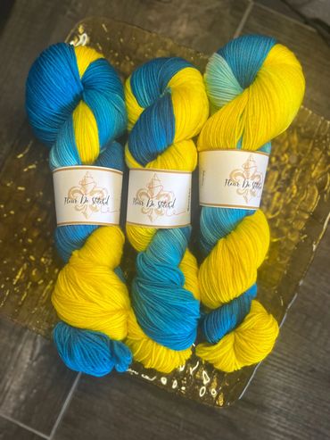 Three skeins of blue and yellow yarn labeled 'Fleur De Stitch'd'.