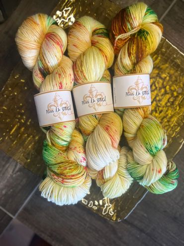 Three skeins of colorful hand-dyed yarn labeled "Fleur De Stitch" on a golden tray.