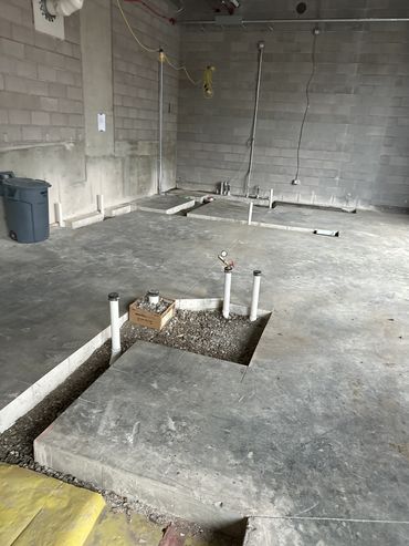 Concrete floor with exposed plumbing and construction materials in an unfinished room.
