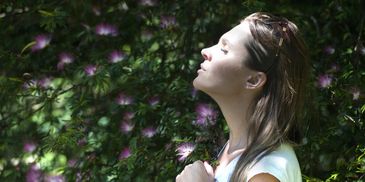 Woman enjoying sunlight with eyes closed near blooming pink flowers.