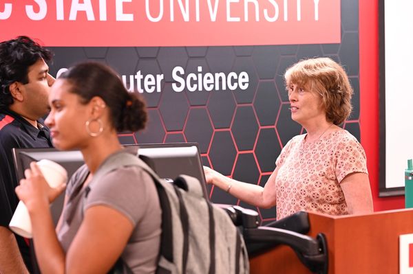Woman speaking to students in a computer science classroom.