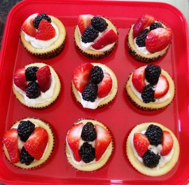 Cupcakes topped with strawberries, blackberries, and cream on a red tray.