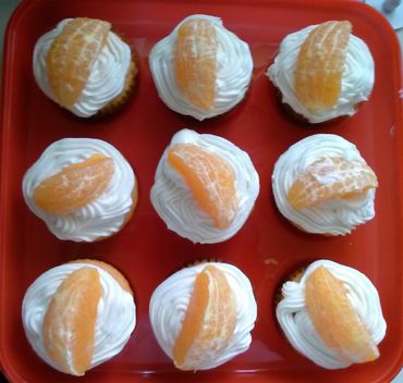 Cupcakes topped with whipped cream and orange slices on a red tray.